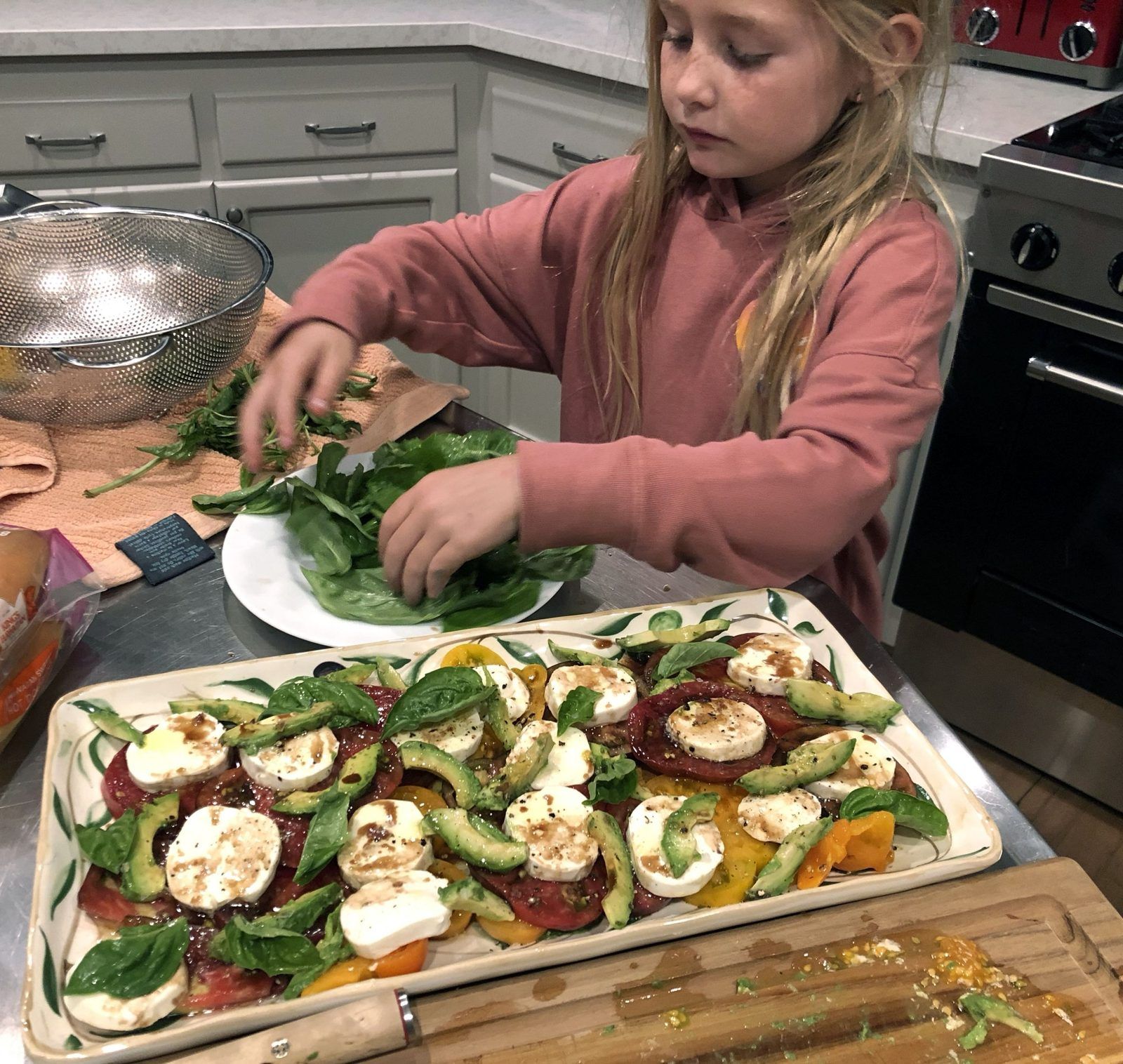 A girl arranging basil over a tomato and mozzarella platter